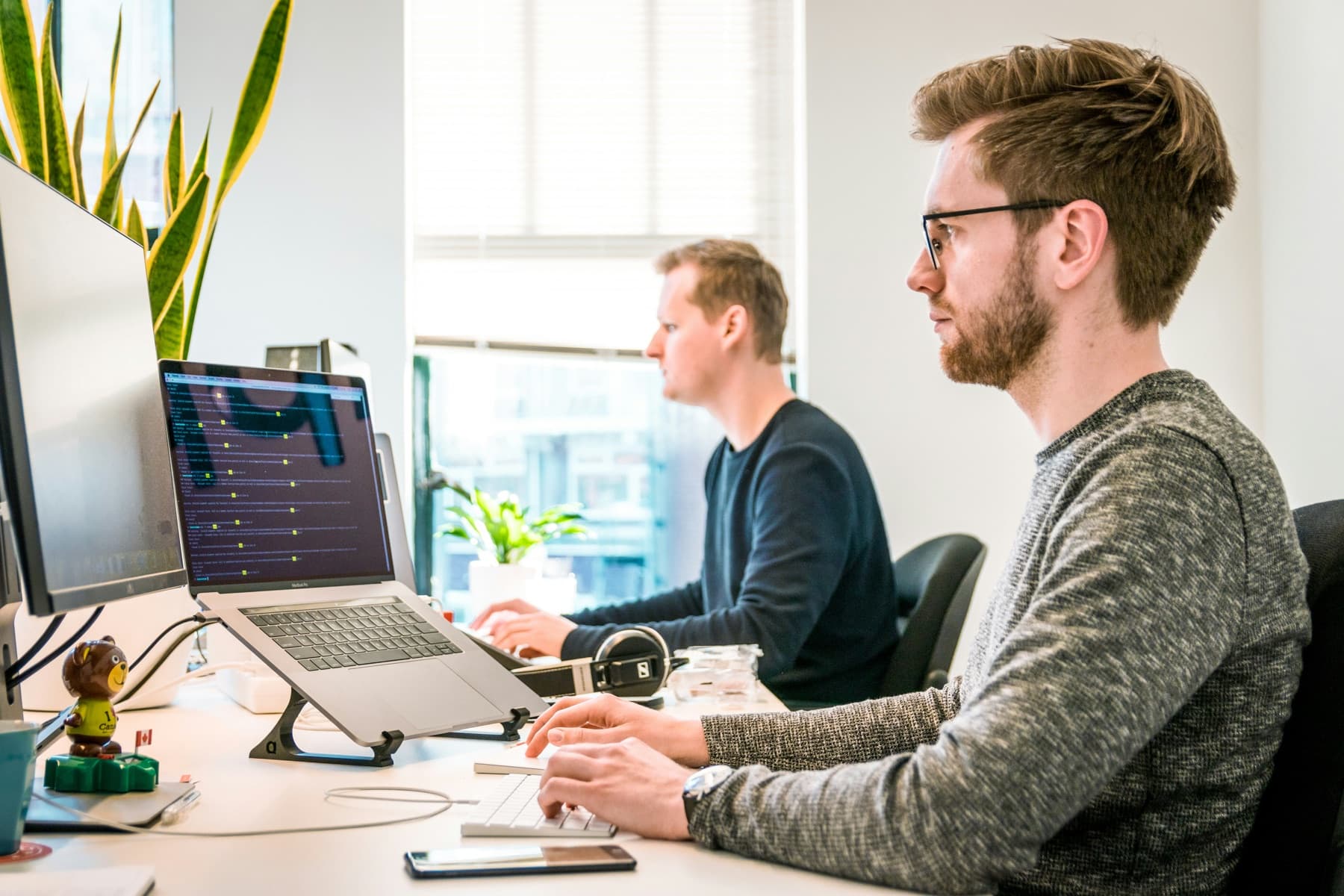 Two people working side by side at desks in a bright agency office