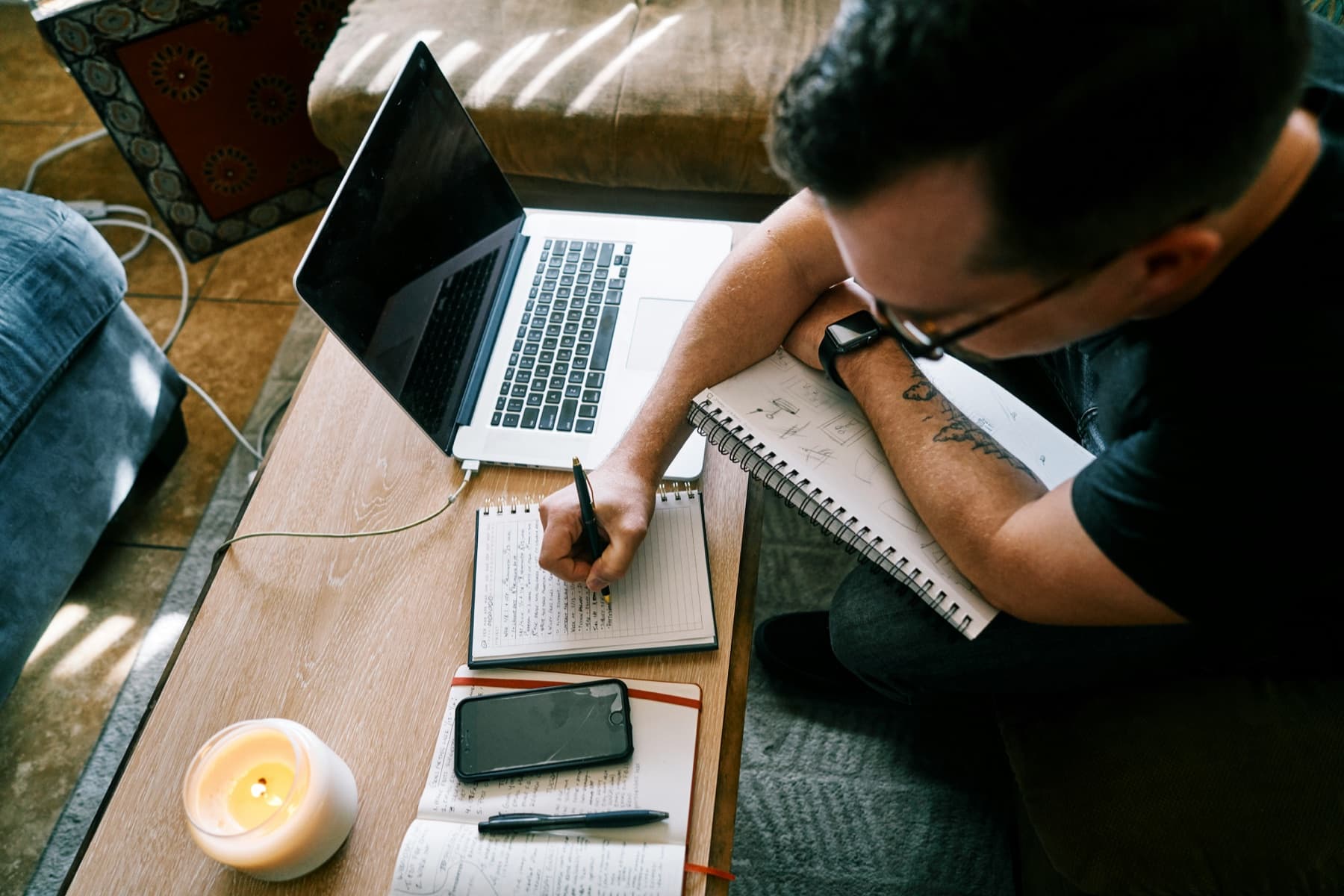 A person writing notes in a notebook beside an open laptop