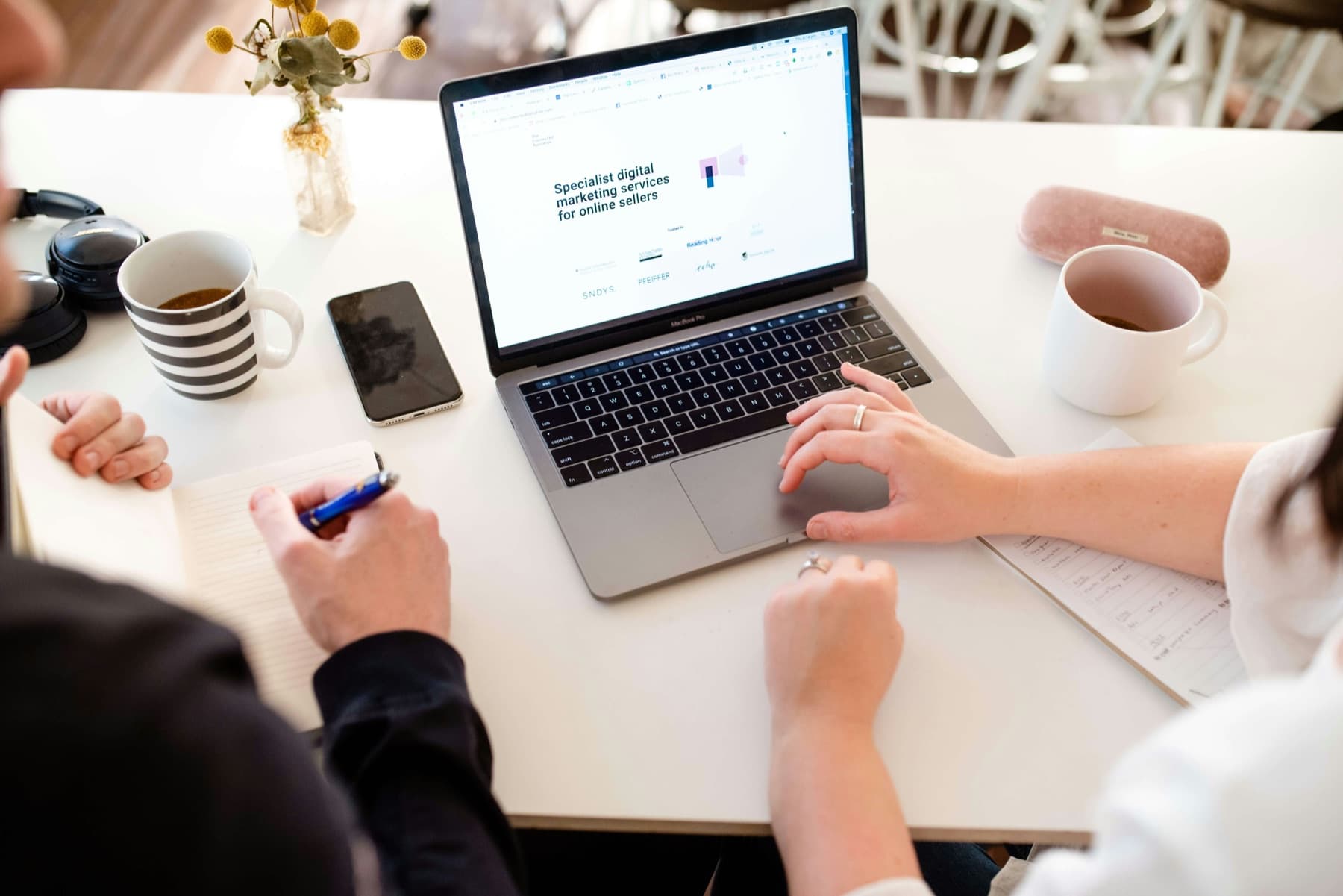 Two people reviewing a marketing report on a laptop over coffee